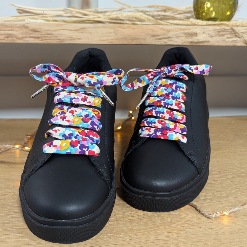 Lacets colorés en tissu fleuri multicolore sur baskets noires, accessoire original et artisanal pour un look vibrant.