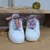 Paire de baskets blanches avec lacets colorés fleuris, accessoire fantaisie pour un look unique et artisanal.